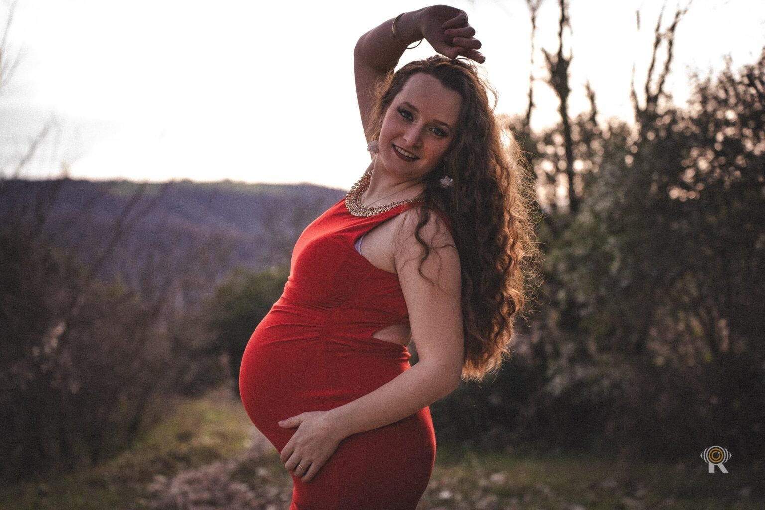 Une femme enceinte sourit, cheveux au vent, à la lumière du soir