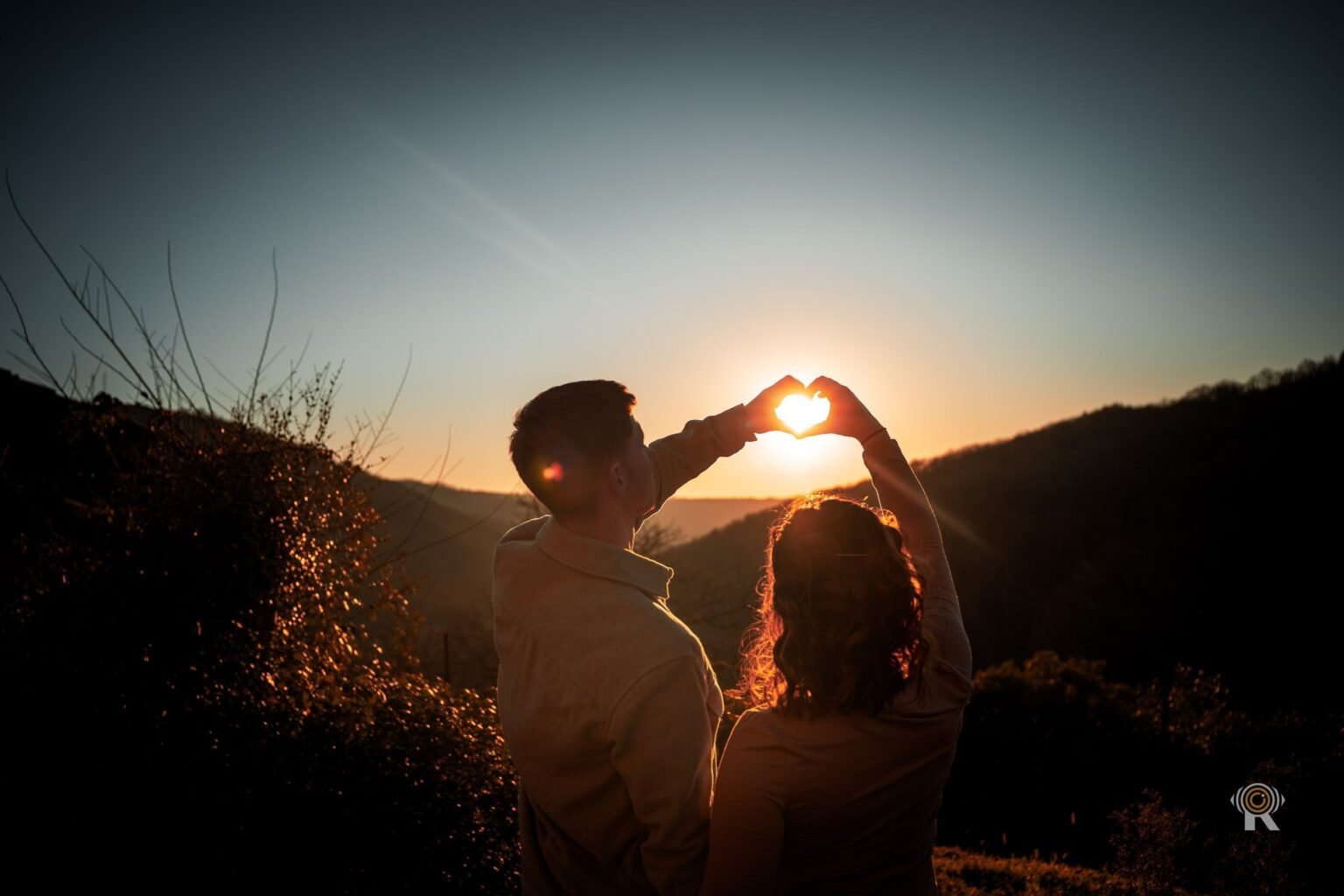 Un couple à contre-jour au coucher du soleil forme un cœur avec ses mains devant l'astre