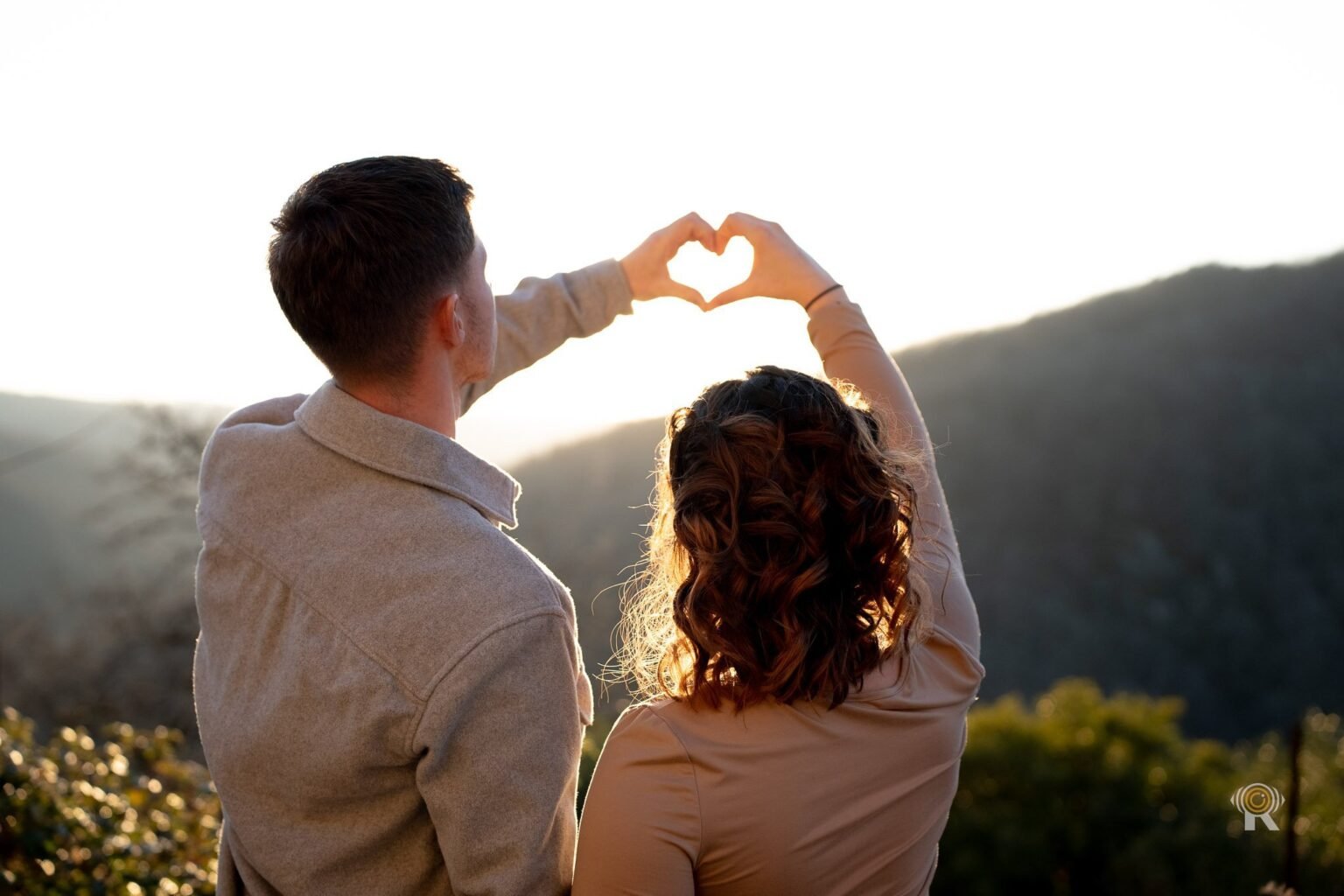 Un couple à contre-jour forme un cœur avec ses mains devant le soleil couchant
