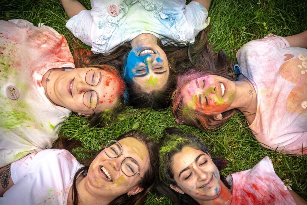 Cercle d’amies allongées dans l’herbe, visages colorés à la poudre, vues du dessus