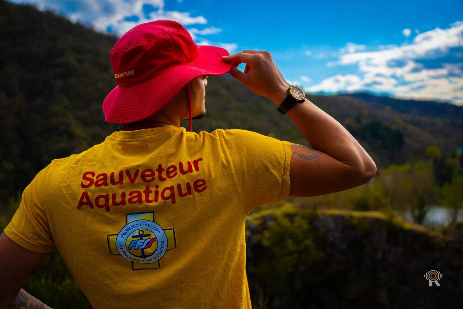 Séance éditoriale : sauveteur aquatique de dos, chapeau rouge et ciel bleu.