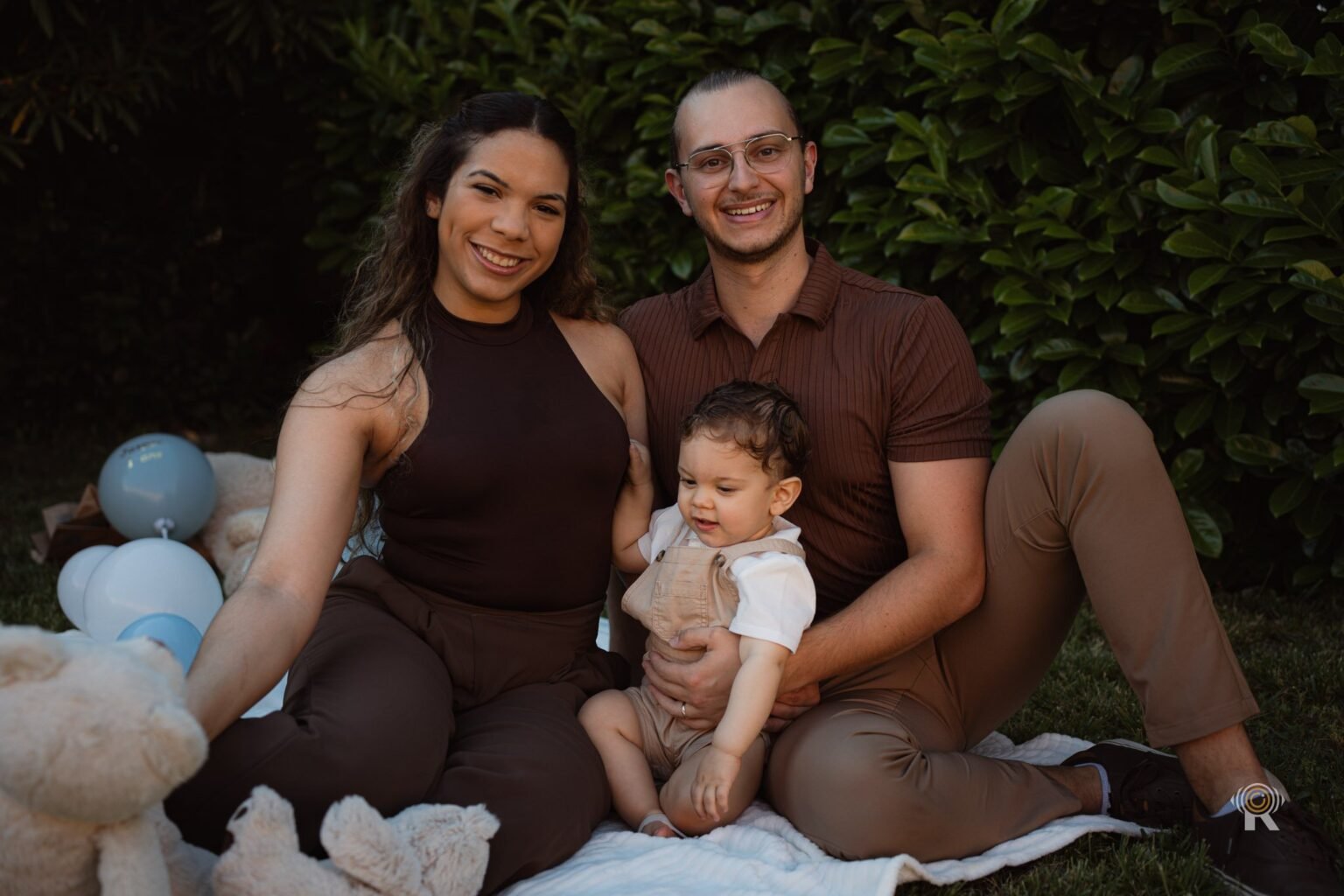 Un couple assis dans l'herbe avec leur bébé et des peluches.