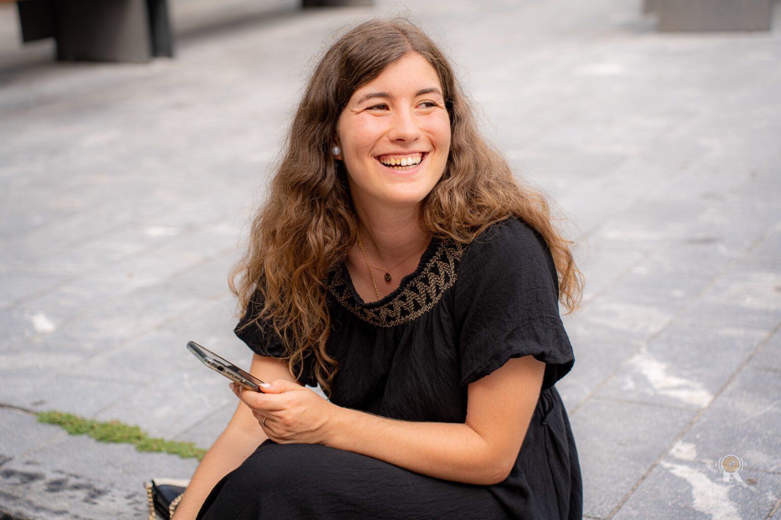 Jeune femme assise dans la rue, elle rit en regardant sur le côté.