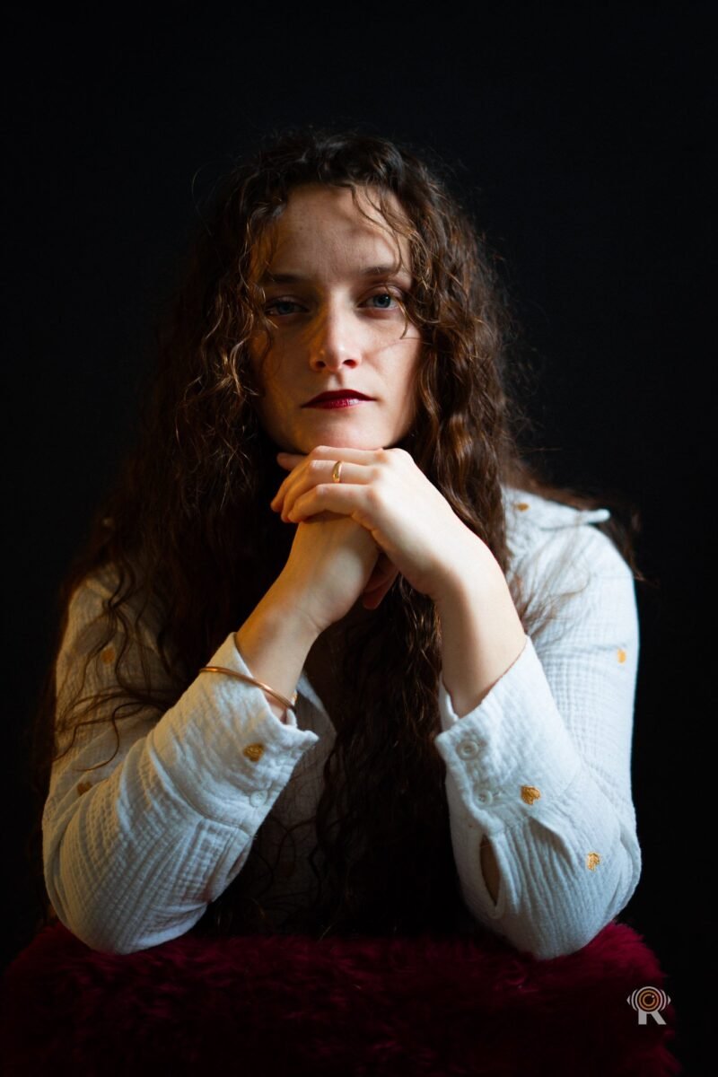 Jennifer Igreja de face, mains jointes sous le menton, bracelet doré au poignet, fond noir
