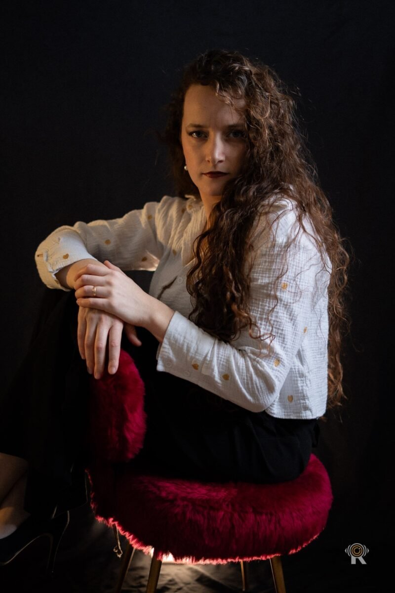 Jennifer Igreja de trois quarts sur un tabouret, regard à l’objectif, mains croisées sur le genou