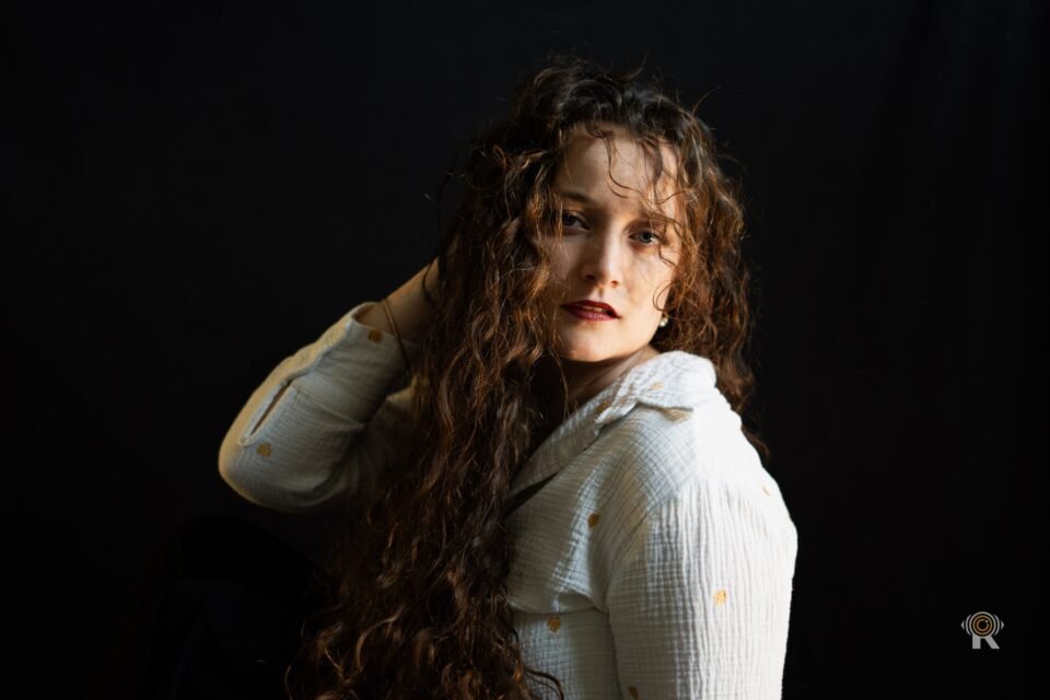 Jennifer Igreja, une main derrière la nuque, buste tourné, regard vers l’objectif, chemise blanche