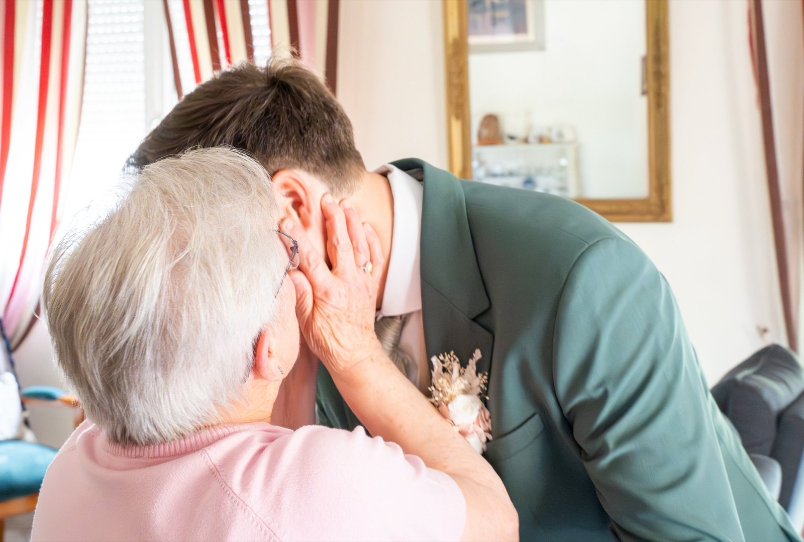 Une grand-mère prend le visage du marié entre ses mains le jour du mariage.