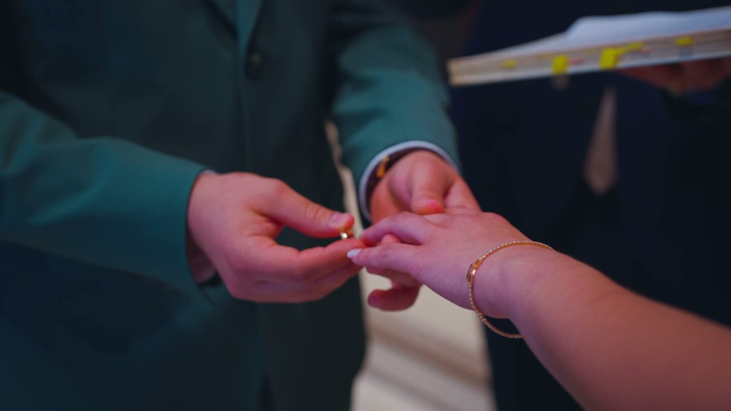 Gros plan sur les mains : le marié passe l’alliance au doigt de la mariée.