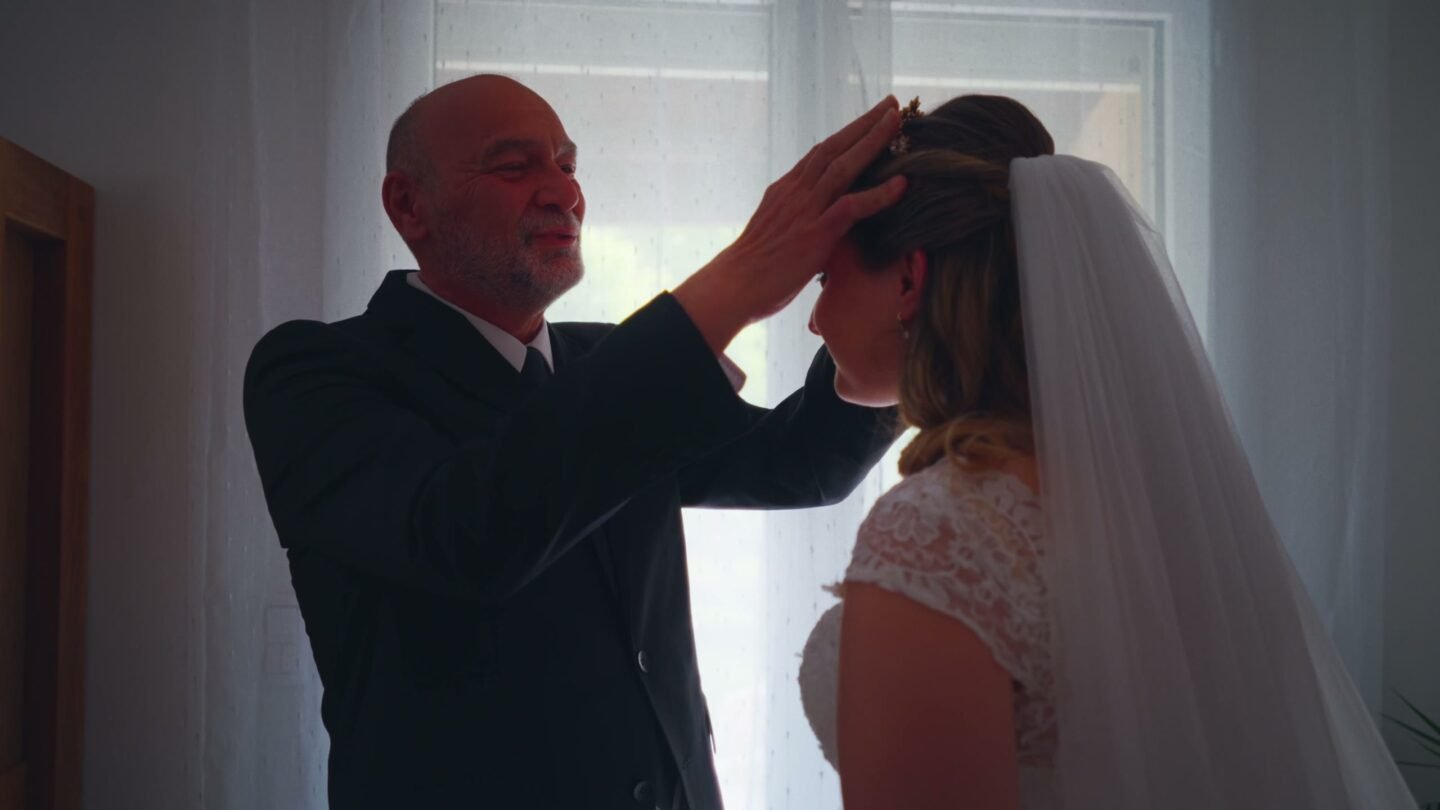 Devant la fenêtre, le père de la mariée pose la main sur sa tête, puis essuie ses larmes.