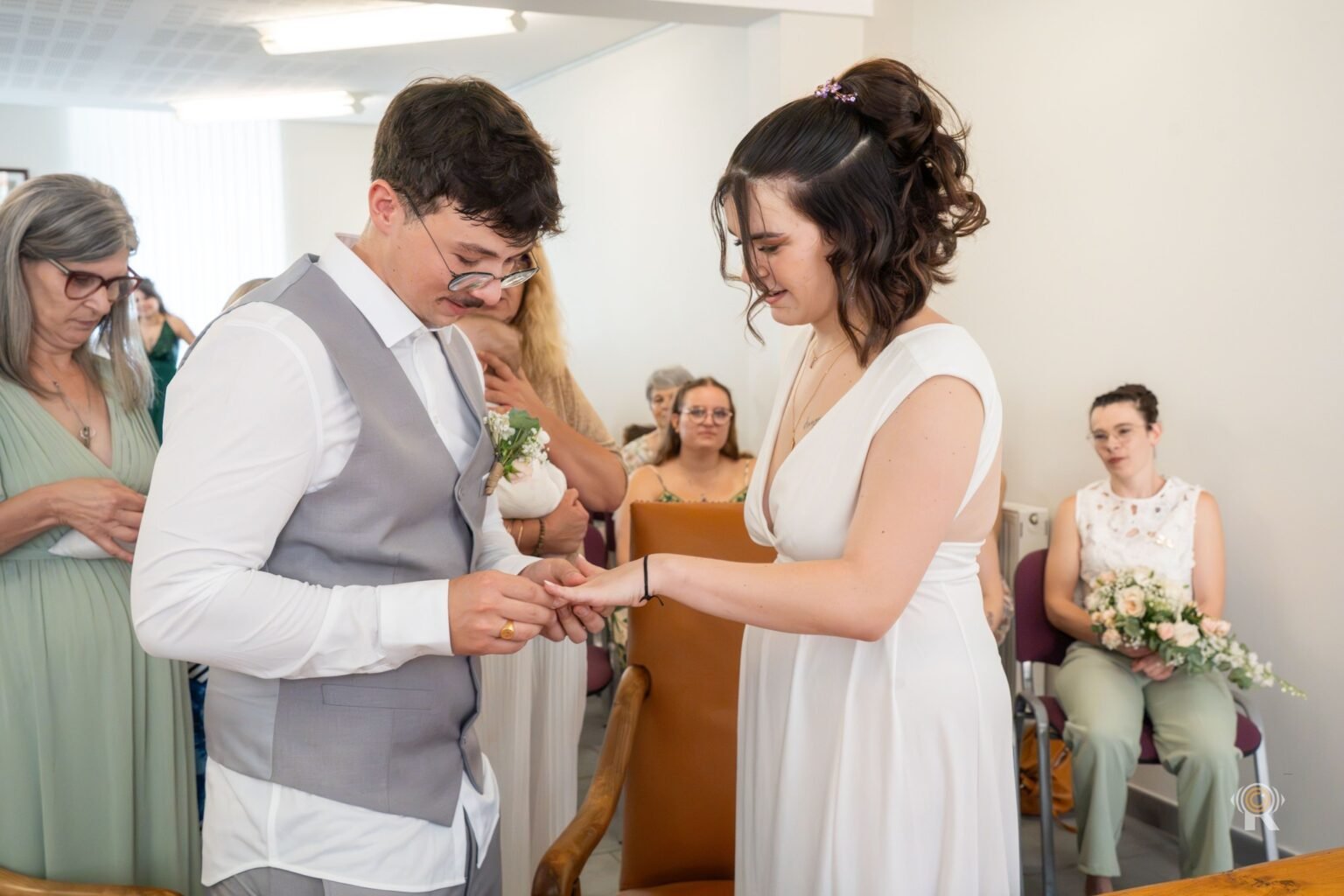 Le marié passe l'alliance à la mariée, les invités assis en mairie