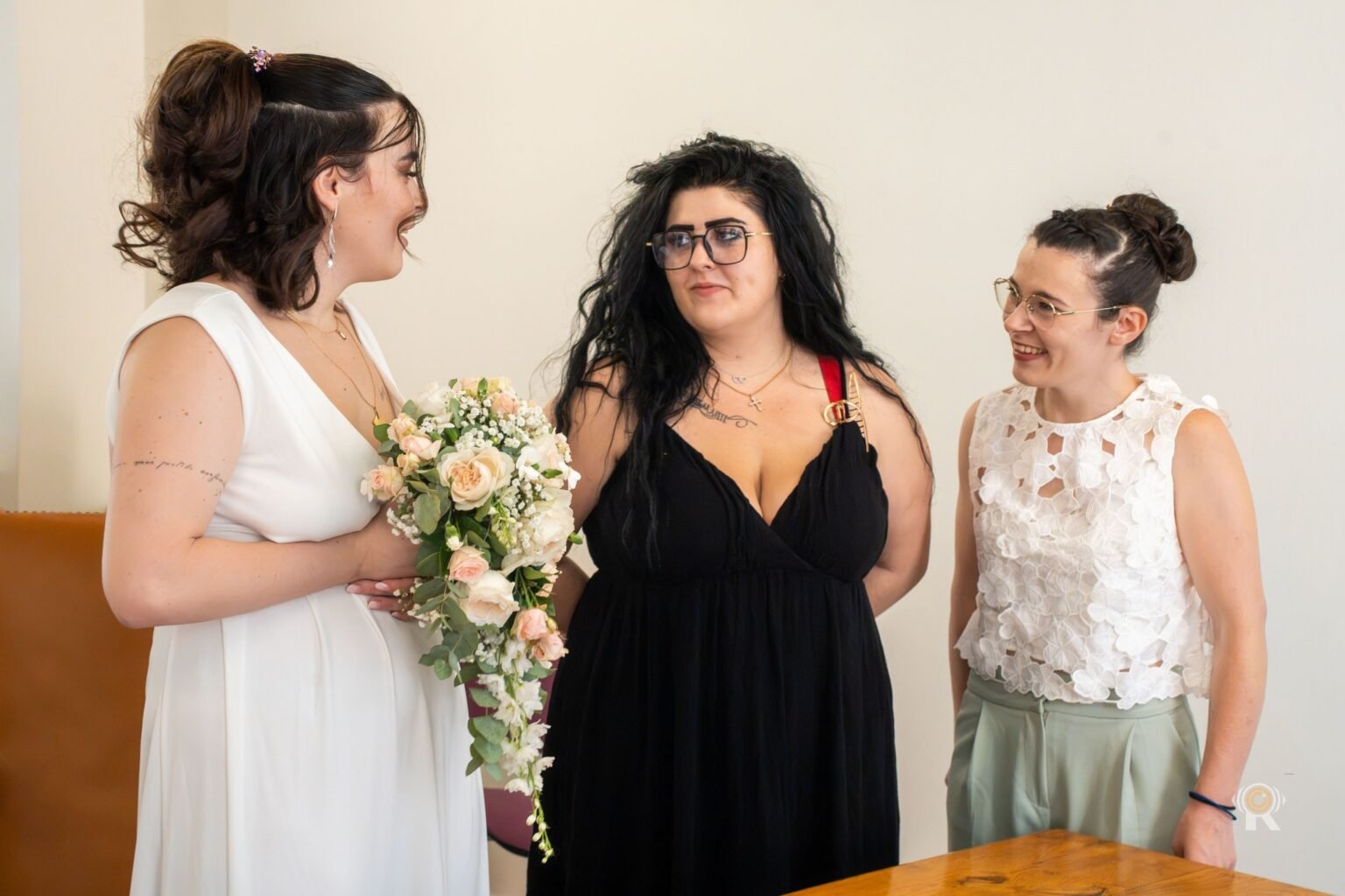 La mariée, son bouquet à la main, entre deux invitées à la mairie