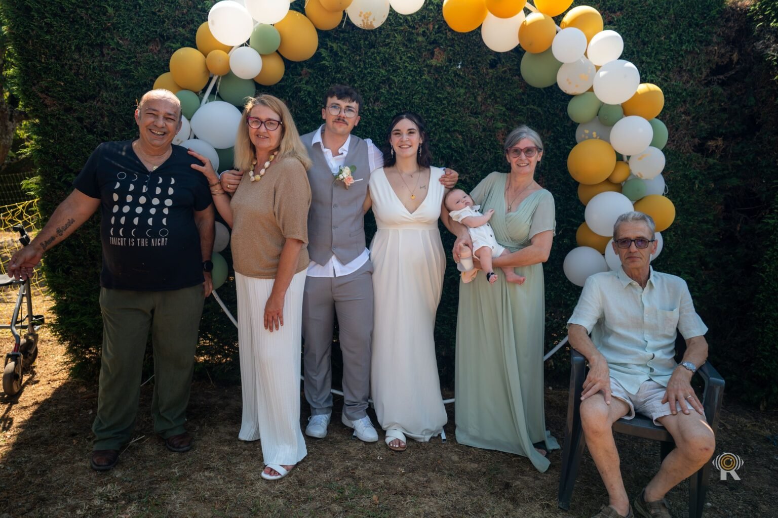 Les mariés entourés de leurs proches devant une arche de ballons