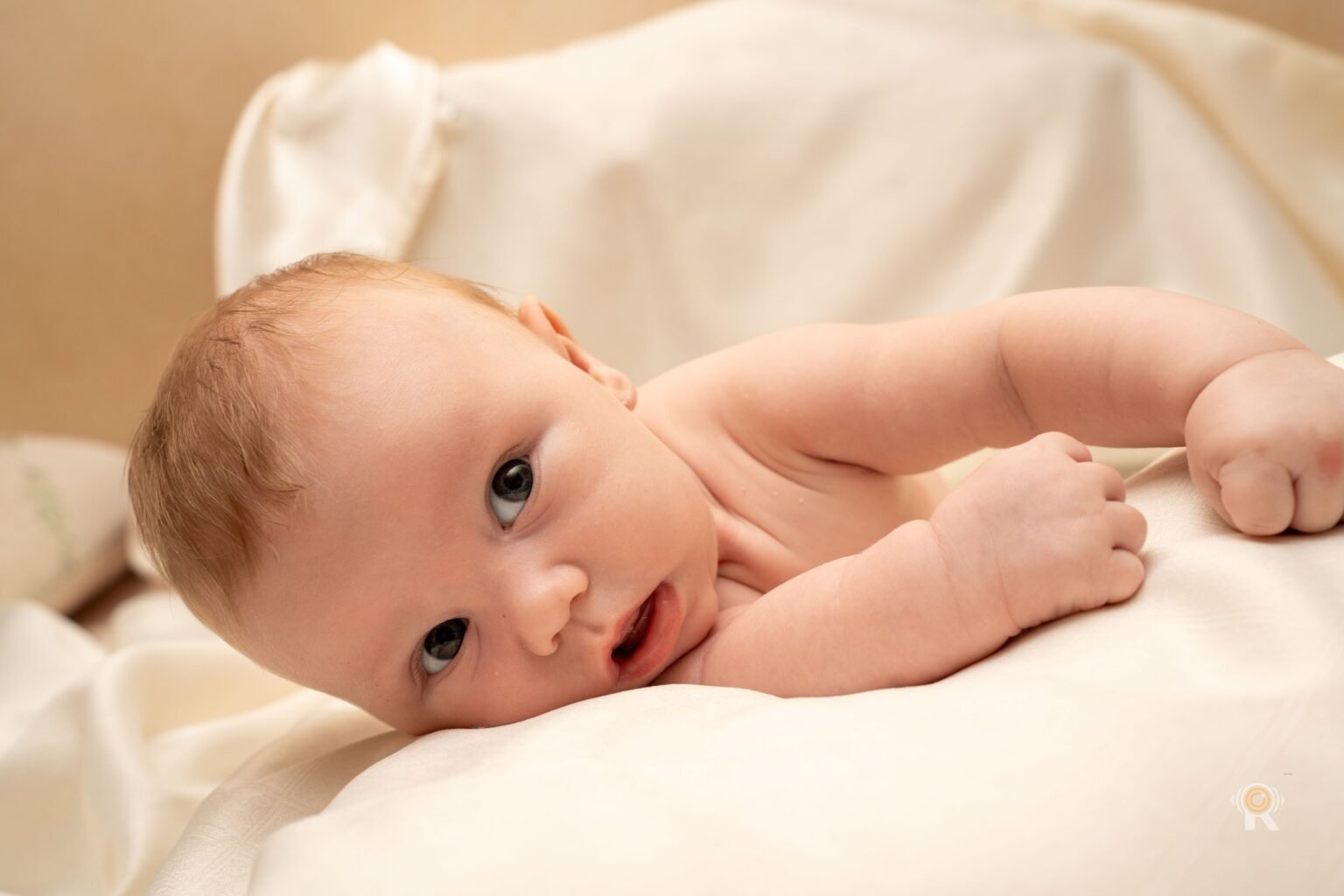 Un bébé éveillé sur un drap clair, à la lumière de la fenêtre