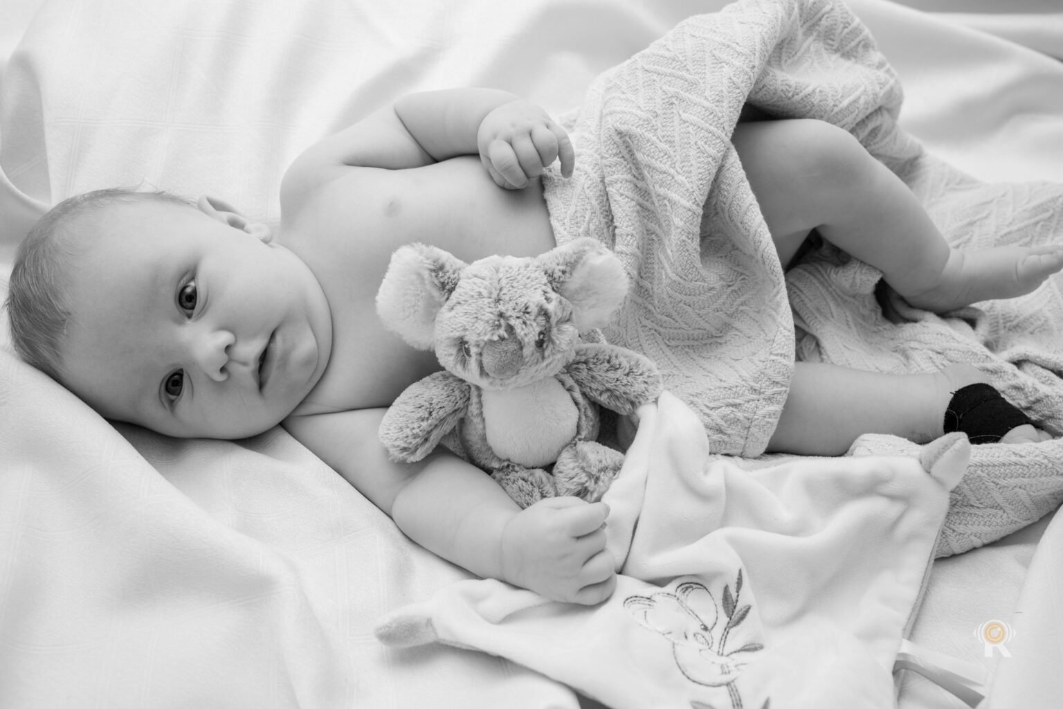 En noir et blanc, un nouveau-né allongé avec sa peluche et son doudou