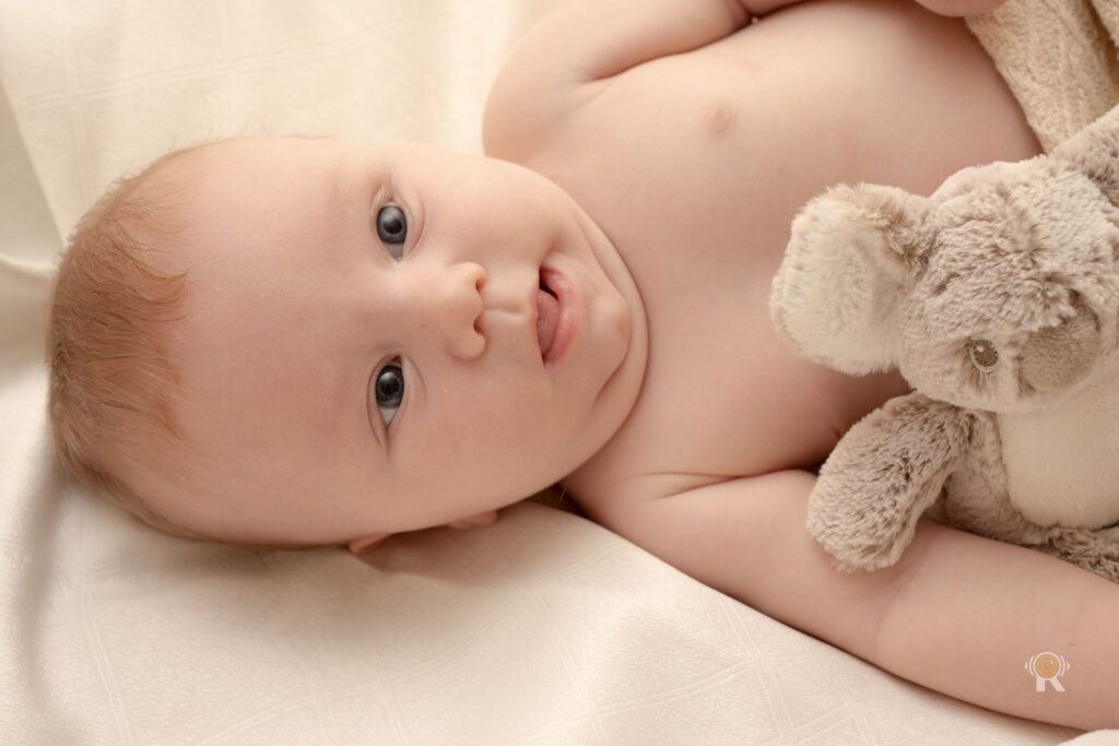 Bébé allongé qui regarde l’objectif, son doudou à côté