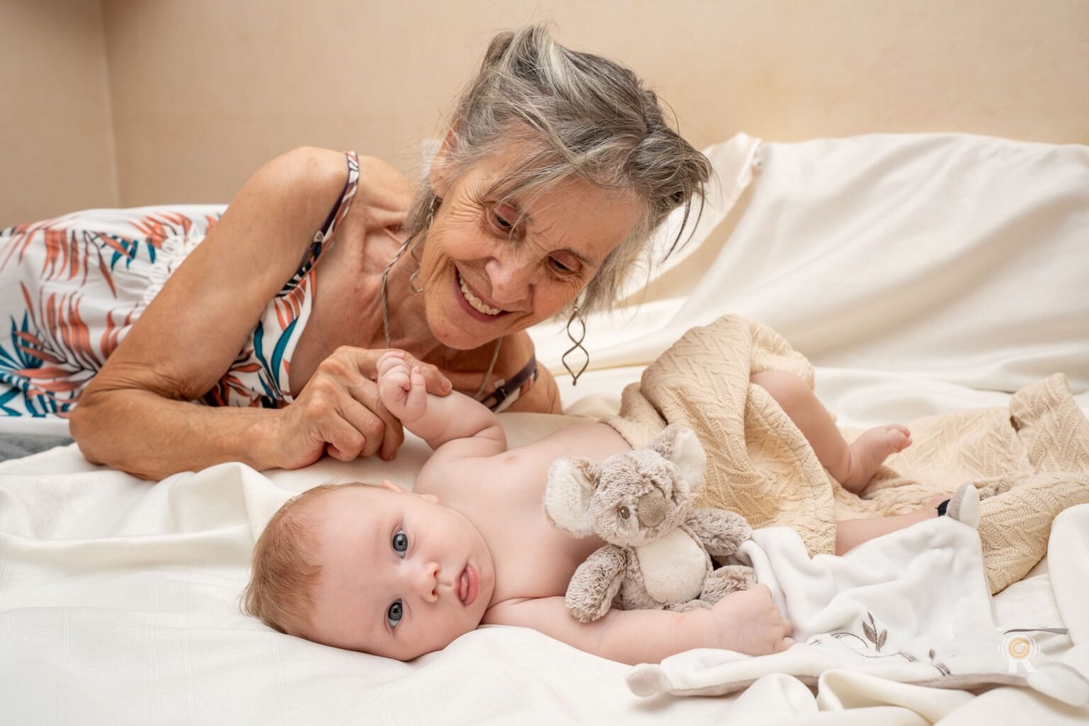 La grand-mère joue avec les mains du nouveau-né sur le lit, lumière de fenêtre