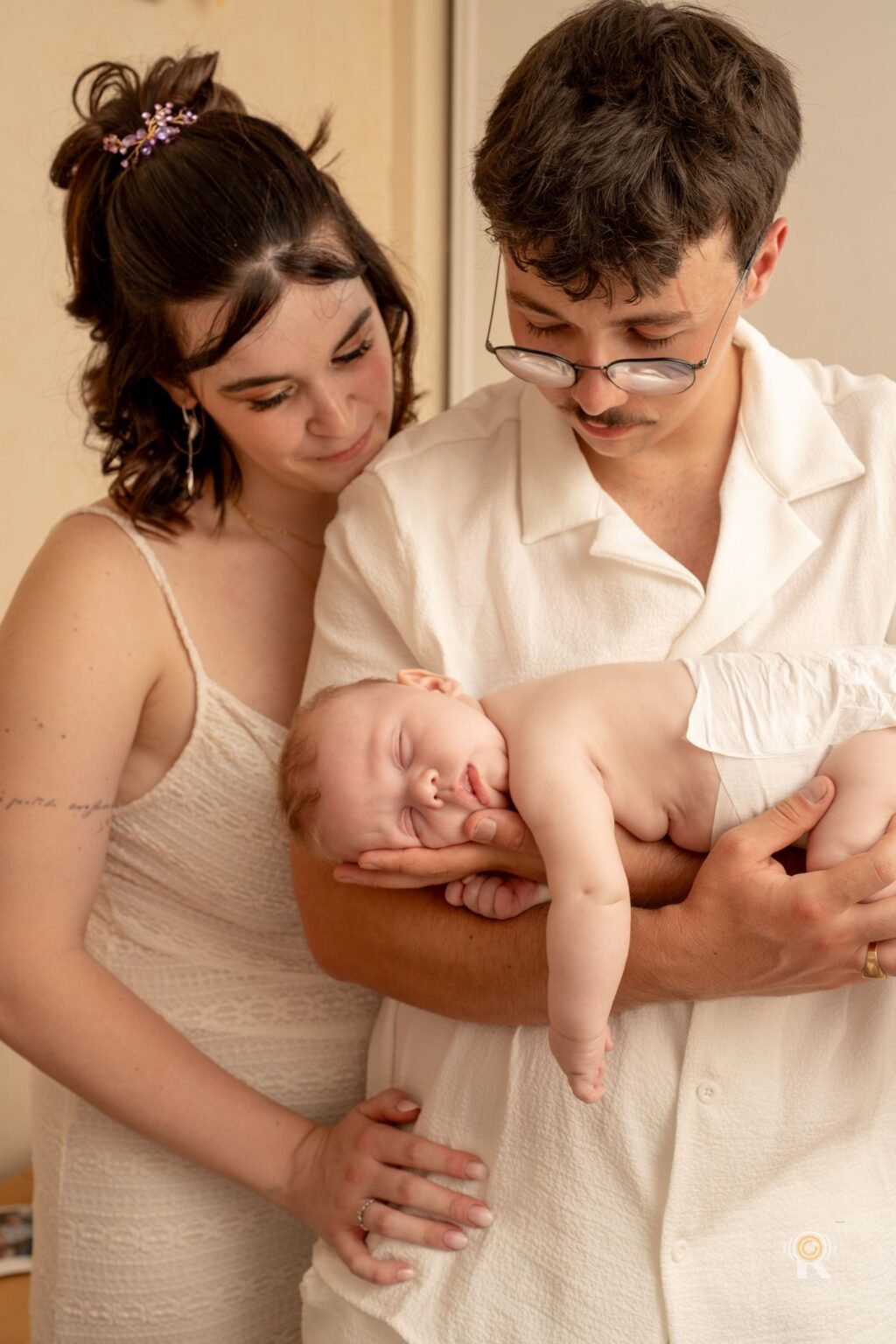 Les parents réunis autour de leur nouveau-né endormi dans les bras du papa, lumière douce à la maison