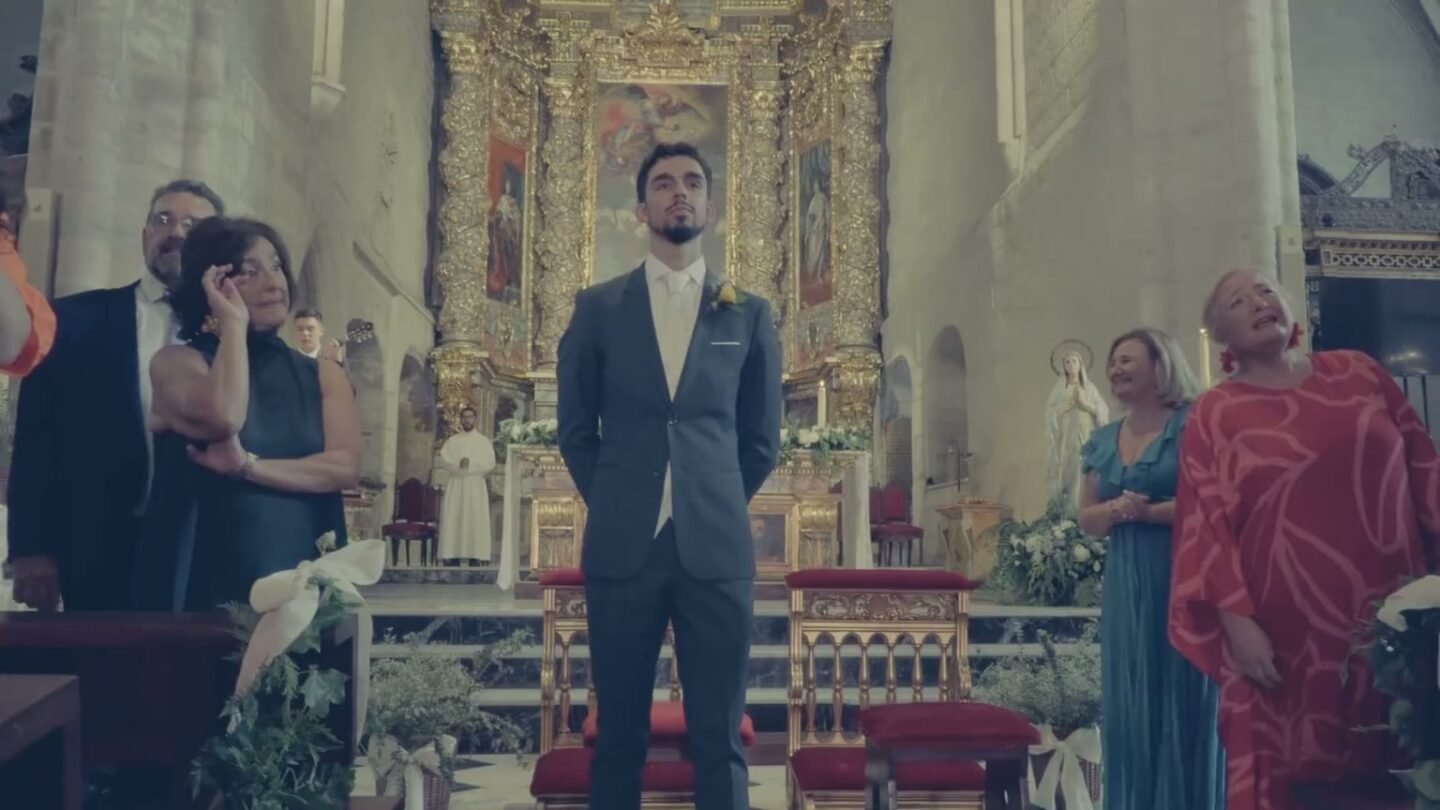 Le marié attend devant le retable doré de l’église, les invités autour de lui.