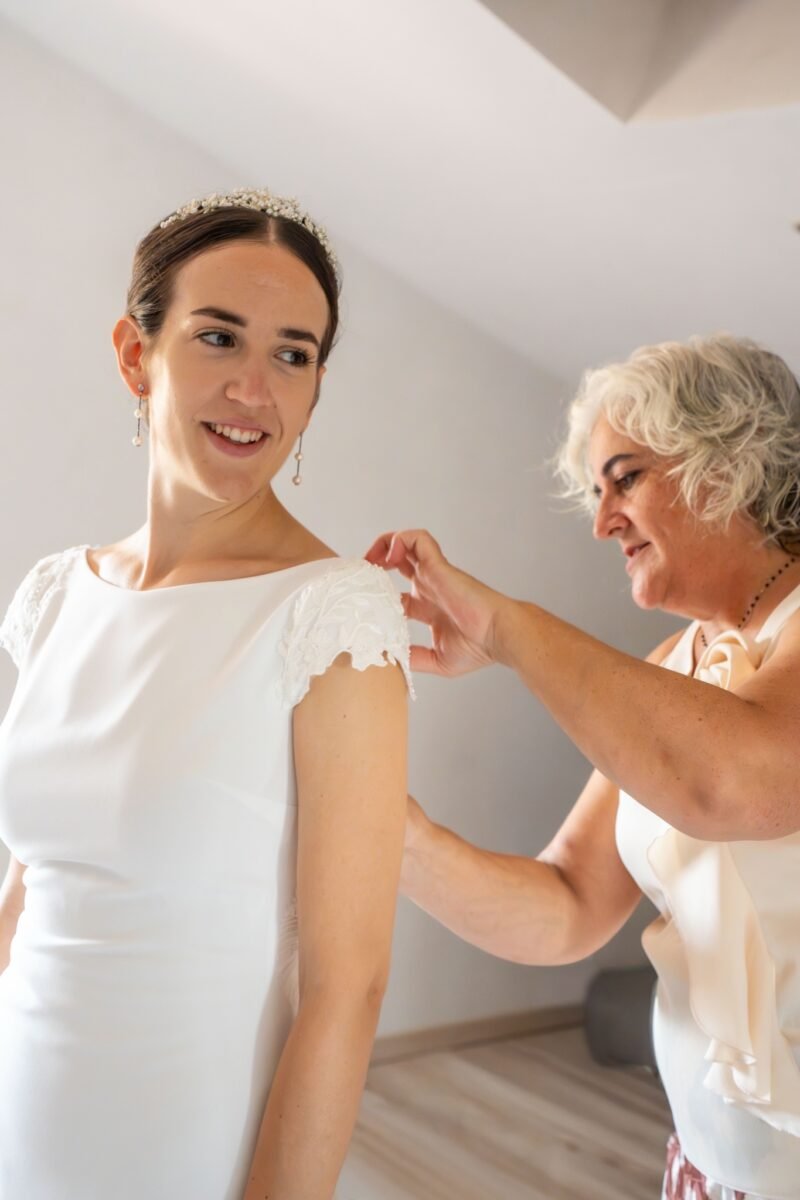 Une proche ajuste la manche de la mariée, qui sourit de côté.