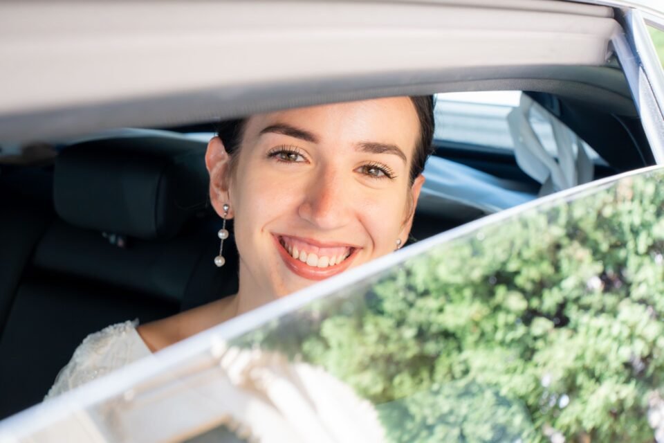La mariée sourit depuis la vitre de la voiture.