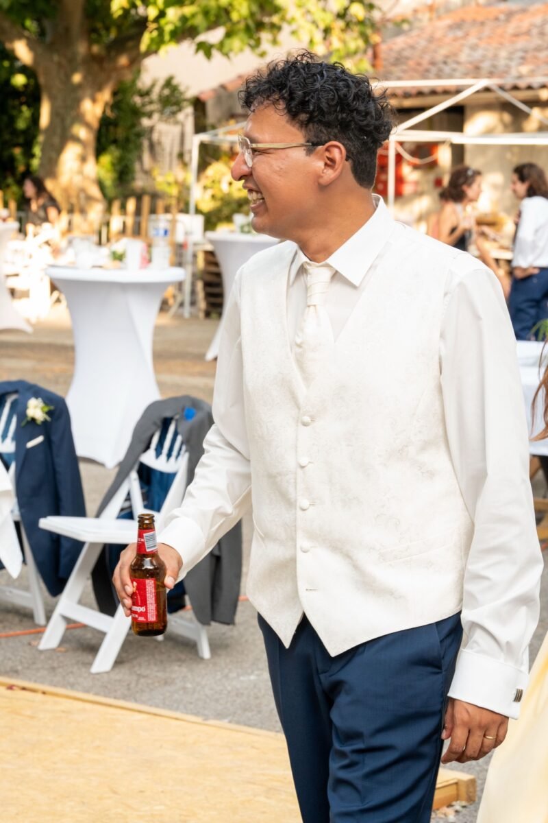 Le marié en gilet, une bière à la main, rit.