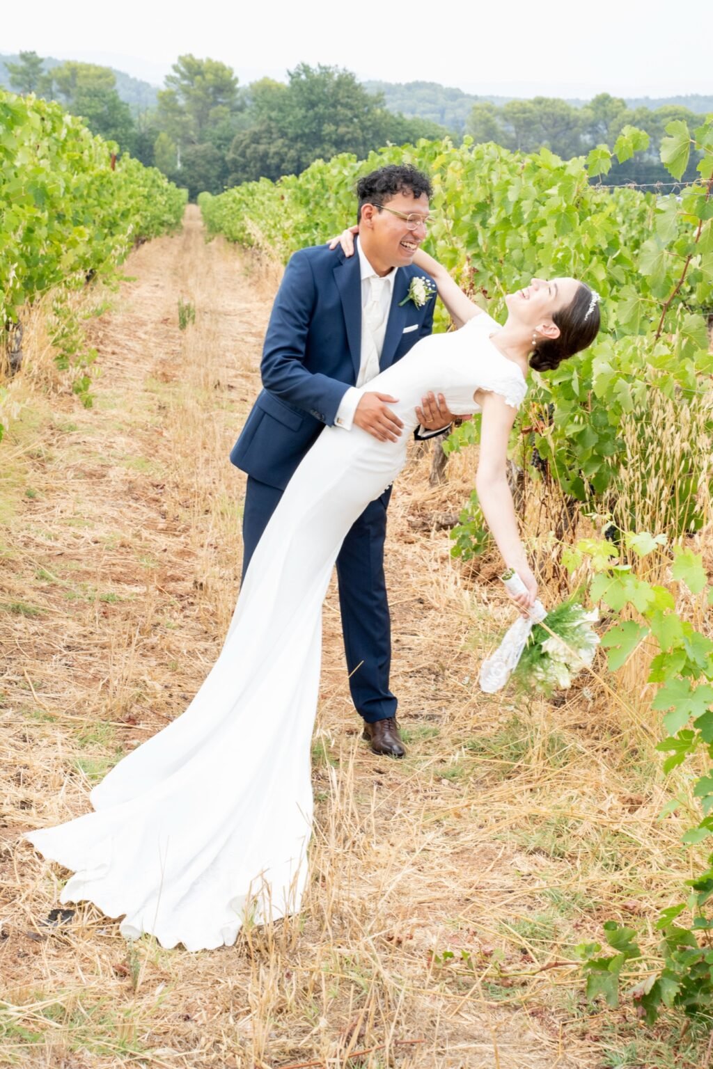 Dans la vigne, elle se penche en arrière en riant pendant qu’il la soutient.